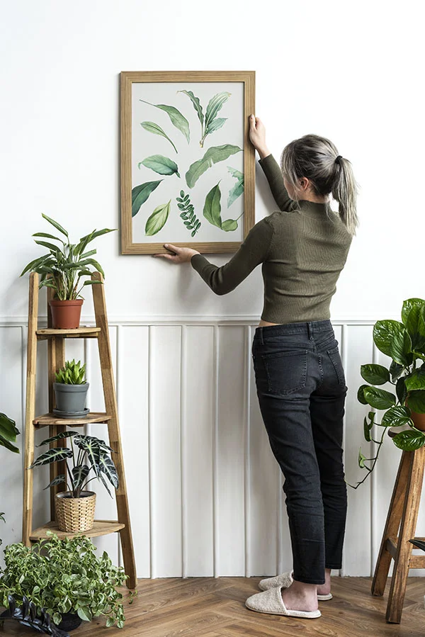 Woman hanging framed botanical artwork on a wall
